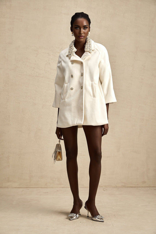 A white woolen coat with embellishments named Fabienne hanging on display