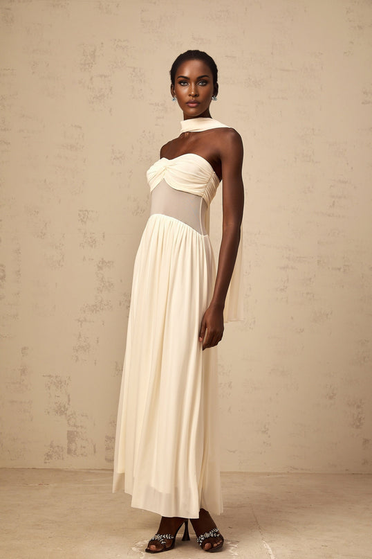A woman wearing a beige midi dress with a scarfinspired mesh design featuring neutral tones and a flowing silhouette