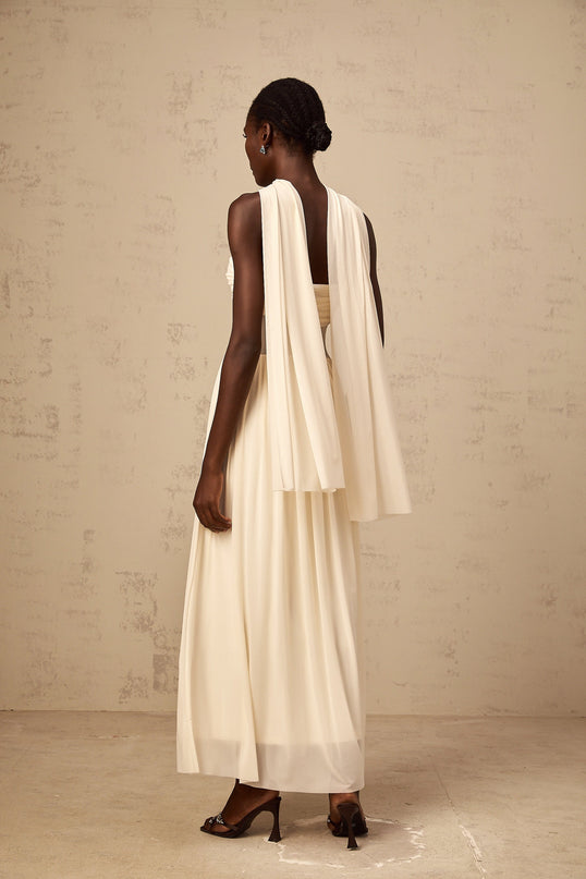 A woman wearing a beige midi dress with a sheer mesh overlay featuring a scarflike pattern in neutral tones The dress has long sleeves and a flowy silhouette