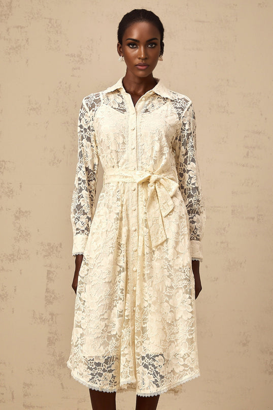 A woman wearing a beige midi length shirt dress with intricate guipure lace detailing standing in a neutral setting