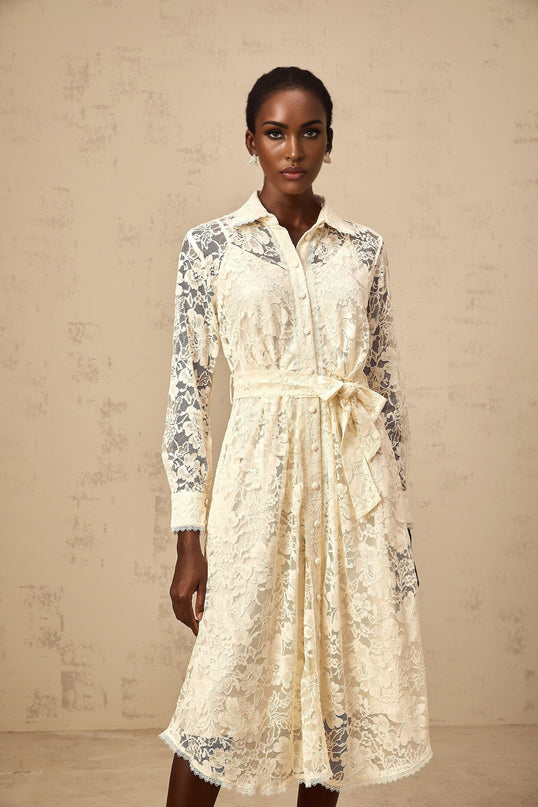 A woman wearing a beige midi shirt dress with intricate guipure lace detailing standing in a neutral background