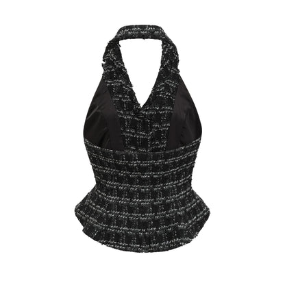 A woman wearing a black and white checked tweed matching set consisting of a sleeveless vest top and a skirt standing against a plain background