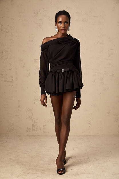 A woman wearing a black asymmetric tulle blouse and matching skirt set The top features a one shoulder design with ruffled details The skirt is flowy and made of tulle fabric The outfit is elegant and suitable for formal occasions