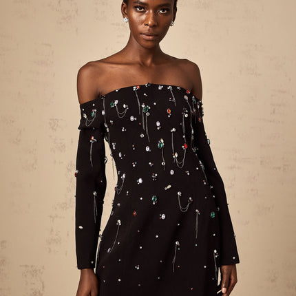 A woman wearing a black crystal embellished offshoulder maxi dress with a fitted bodice and flowing skirt