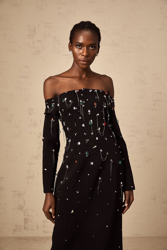 A woman wearing a black crystal embellished offshoulder maxi dress with a fitted bodice and flowing skirt