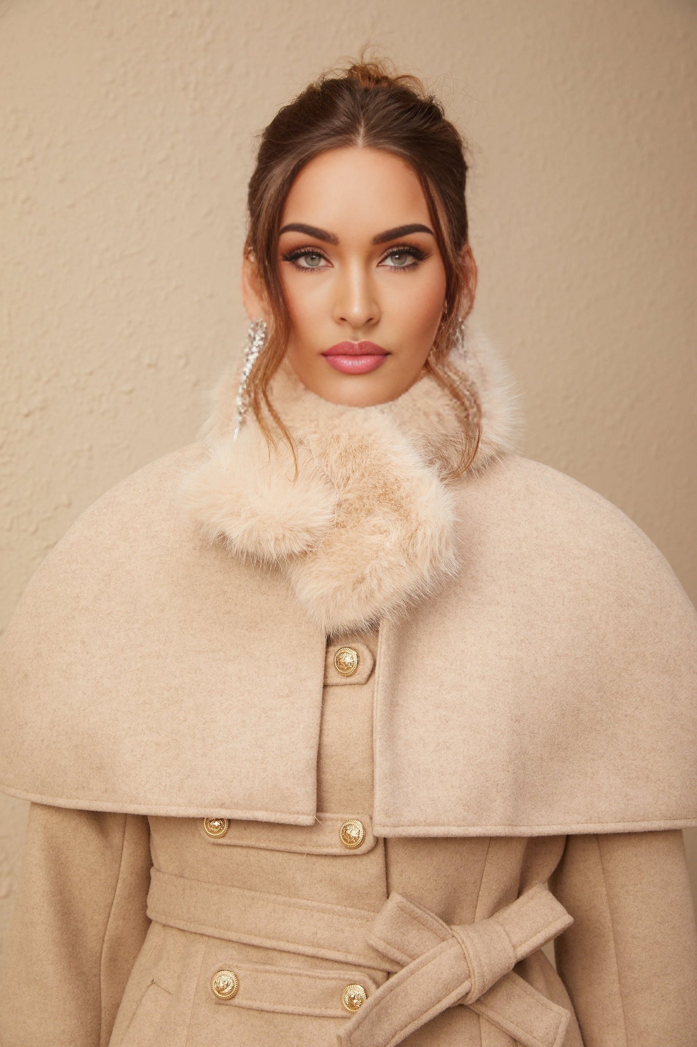 A woman wearing a black faux fur coat with a detachable cape collar standing against a plain background