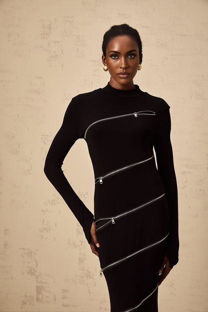 A woman wearing a black fitted maxi dress with zipper details standing against a plain background