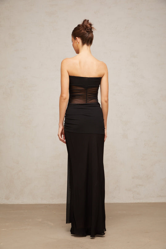 A woman wearing a black floorlength dress with a pleated tulle skirt and semisheer details standing in a neutral pose