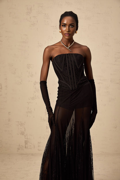 A woman wearing a black floral lace corset matching skirt and gloves set with delicate lace patterns and a fitted silhouette