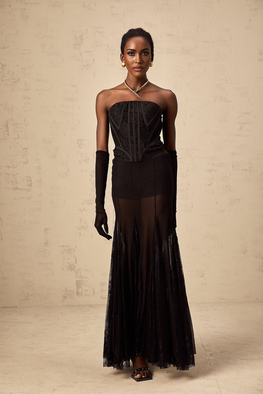 A woman wearing a black floral lace corset skirt and gloves set named Violaine The ensemble features delicate lace patterns and a matching design for all three pieces