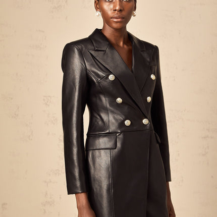 A woman wearing a black leather blazer mini dress with long sleeves and a tailored fit standing against a plain background