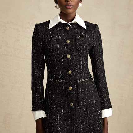 A woman wearing a black mini dress with a tweed fabric base and sequin panels standing against a plain background