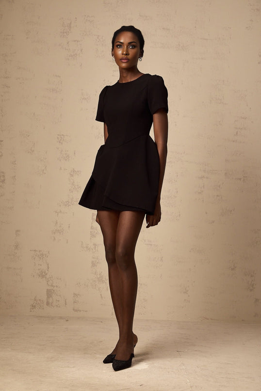 A woman wearing a black mini dress with an asymmetric neckline and ruffled detailing