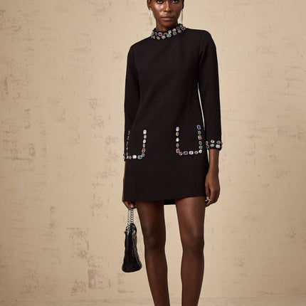 A woman wearing a black mini dress with long sleeves adorned with crystal embellishments standing in an elegant pose