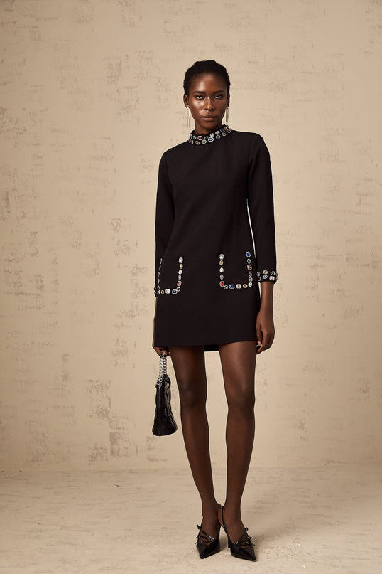 A woman wearing a black mini dress with long sleeves adorned with crystal embellishments standing in an elegant pose