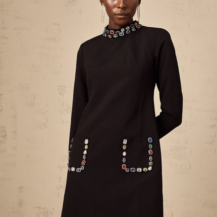 A woman wearing a black mini dress with long sleeves adorned with crystal embellishments