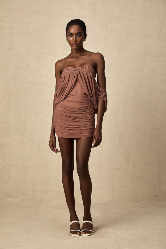 A woman wearing a black offshoulder bodysuit paired with a matching black skirt standing in a neutral pose