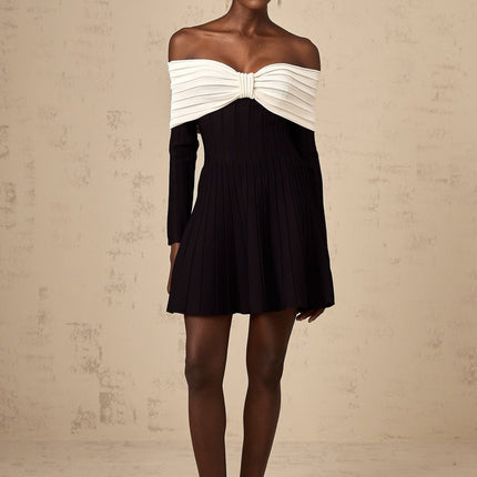 A woman wearing a black offshoulder mini dress with a bow detail and knit fabric