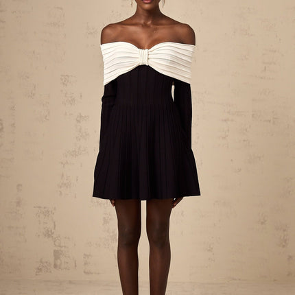 A woman wearing a black offshoulder mini dress with a bow detail and knit fabric