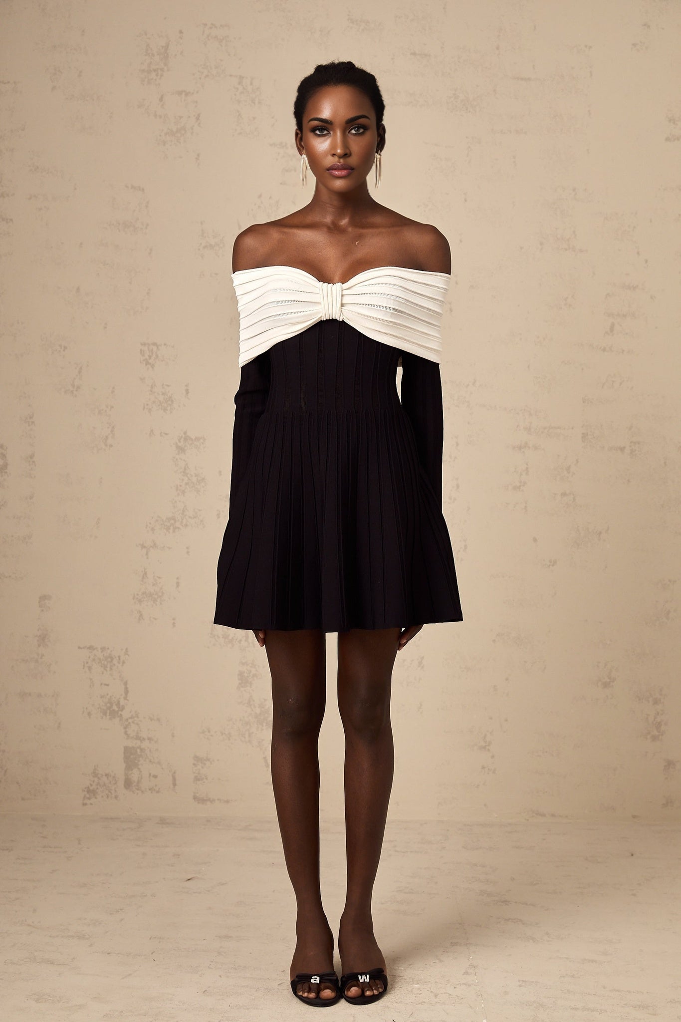 A woman wearing a black offshoulder mini dress with a bow detail and knit fabric