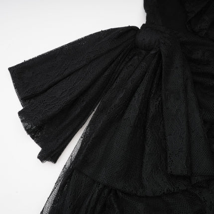 A woman wearing a black oneshoulder maxi dress with a cutout detail standing against a plain background