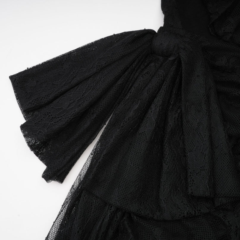 A woman wearing a black oneshoulder maxi dress with a cutout detail standing against a plain background