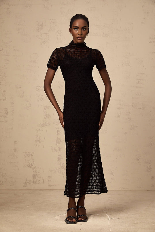 A woman wearing a black semisheer knit midi dress standing against a neutral background
