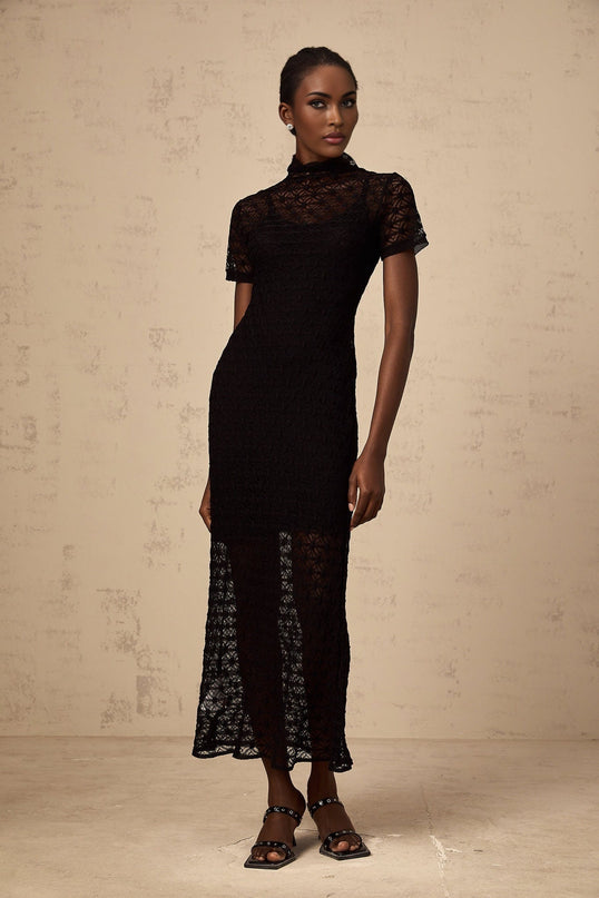 A woman wearing a black semisheer knit midi dress with a formfitting silhouette standing against a plain background