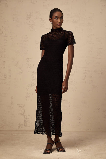 A woman wearing a black semisheer knit midi dress with a formfitting silhouette standing against a plain background