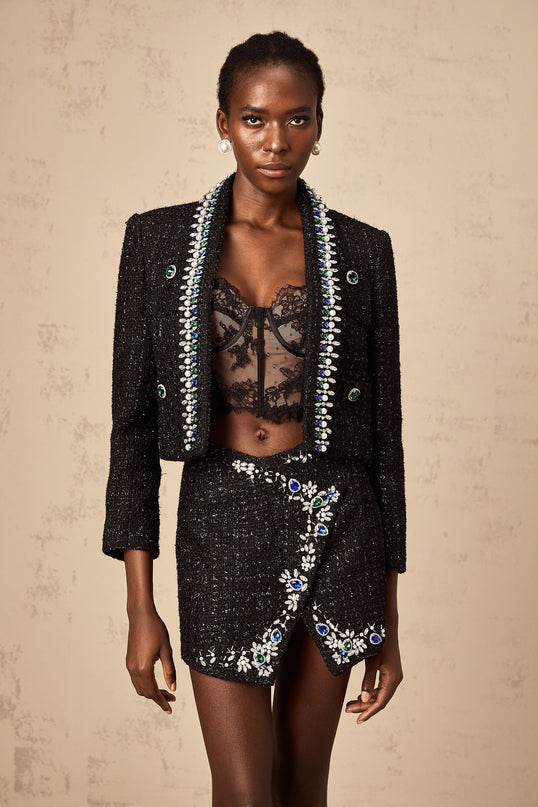 A woman wearing a black tweed jacket and matching skirt set with crystal embellishments the outfit has a classic and elegant appearance