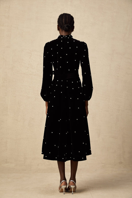 A woman wearing a black velvet midi dress with embellishments standing in a neutral background
