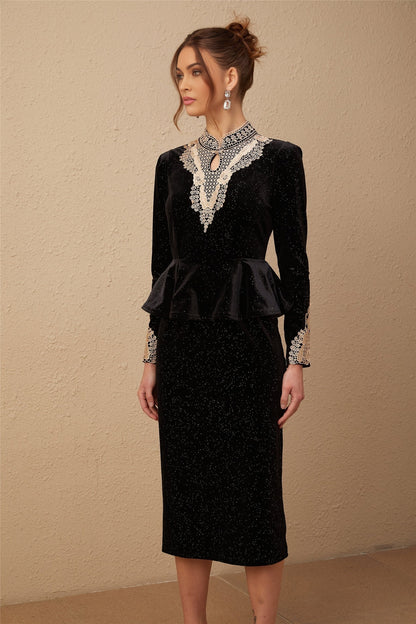 A woman wearing a black velvet midi dress with embellishments standing in a neutral pose against a plain background