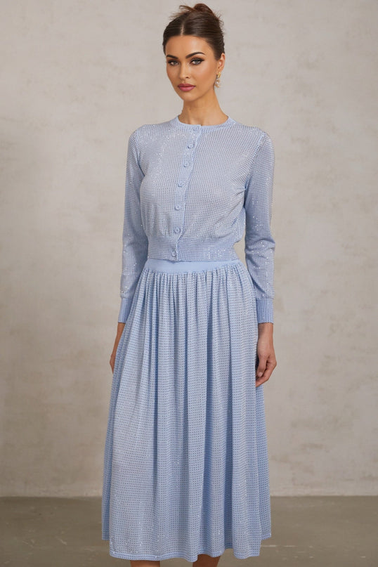 A woman wearing a blue knitted two piece outfit consisting of a sleeveless top and skirt adorned with sparkling rhinestones The set has a fitted silhouette and shimmering texture