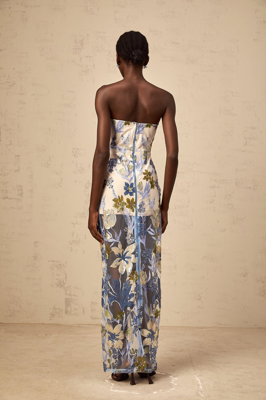 A woman wearing a blue maxi dress with sequined flower embroidery and a corset bodice featuring tulle detailing