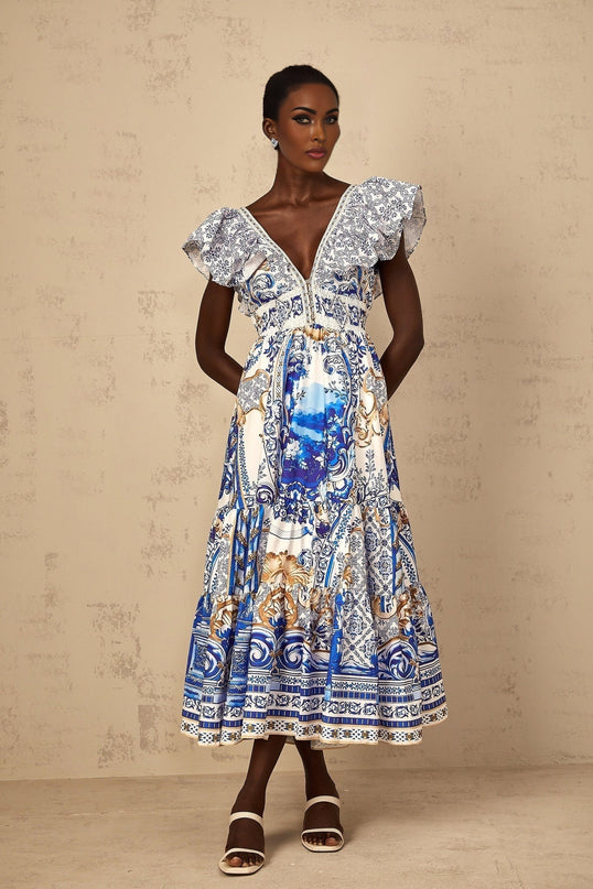 A woman wearing a blue midi dress with a baroque print pattern and tiered skirt design