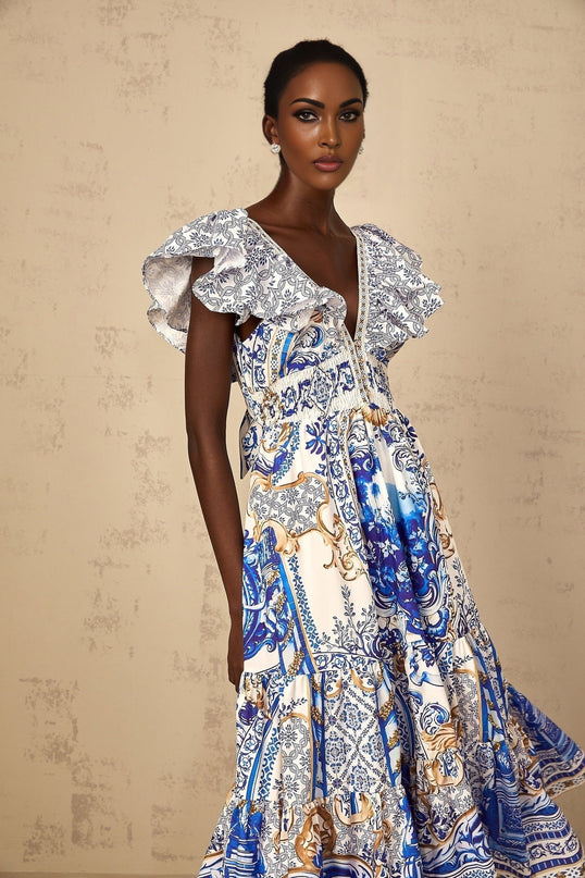 A woman wearing a blue midi dress with a baroque print pattern and tiered skirt design