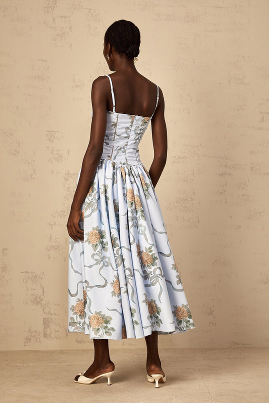 A woman wearing a blue midi dress with a floral print pattern standing against a plain background