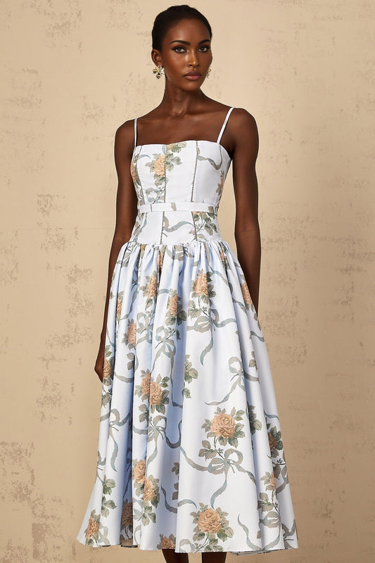 A woman wearing a blue midi dress with a floral print pattern standing in a relaxed pose