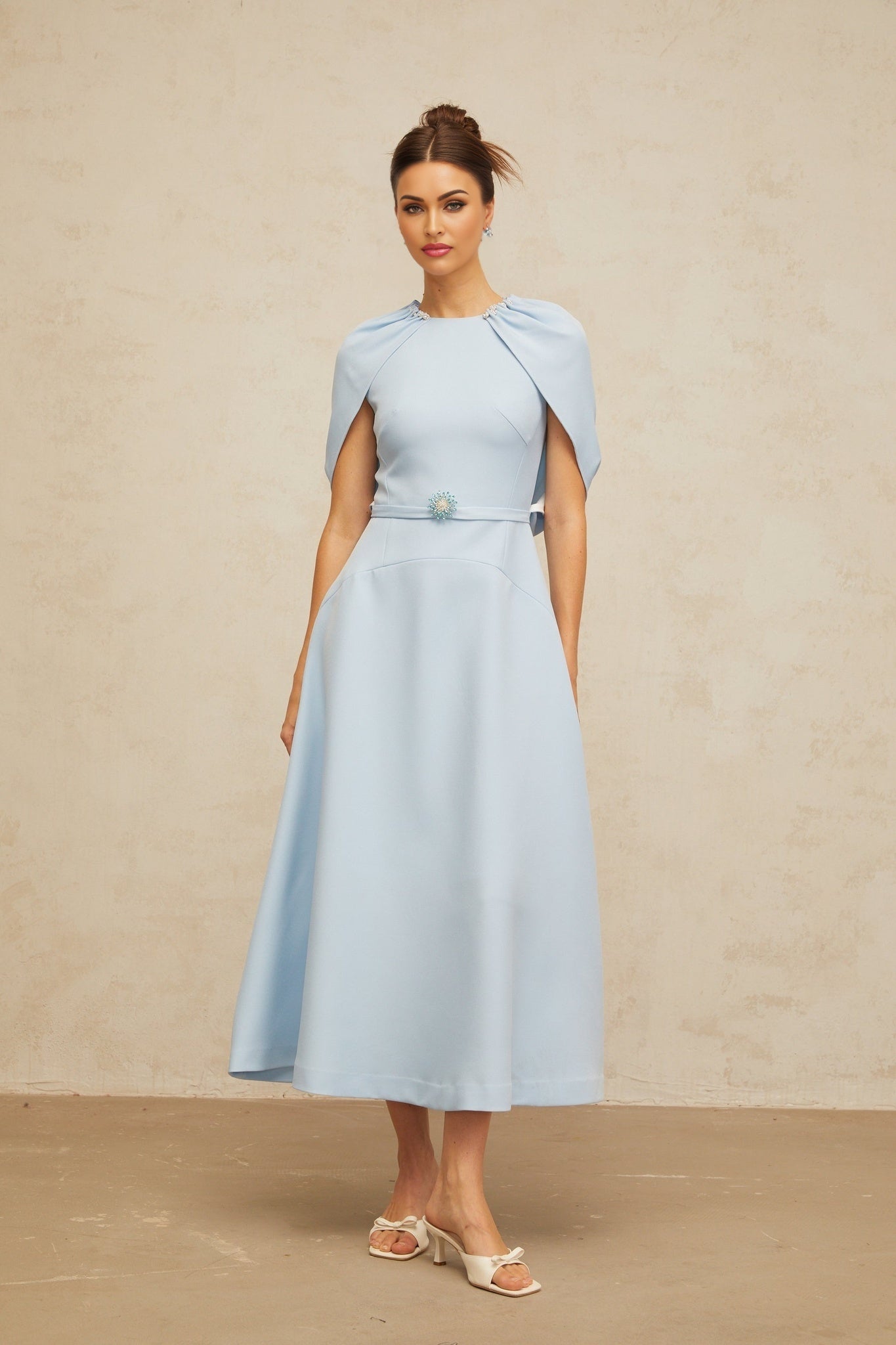 A woman wearing a blue midi dress with shawl panels and embellishments