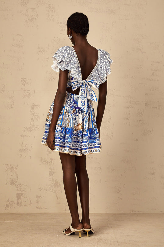 A woman wearing a blue mini dress with a baroque print pattern and tiered skirt design