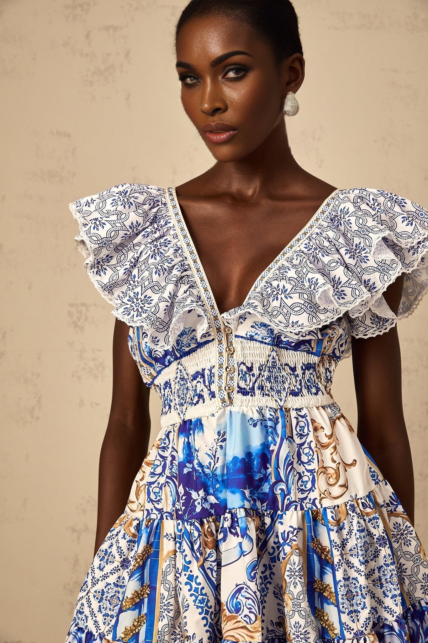 A woman wearing a blue mini dress with a baroque print pattern and tiered skirt design