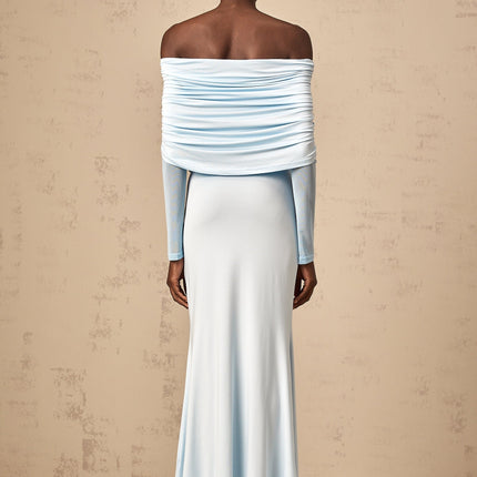 A woman wearing a blue offshoulder maxi dress with ruched detailing standing against a plain background