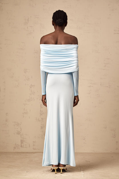 A woman wearing a blue offshoulder maxi dress with ruched detailing standing against a plain background