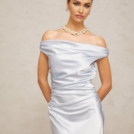 A woman wearing a blue offshoulder maxi dress with ruched satin fabric standing against a plain background