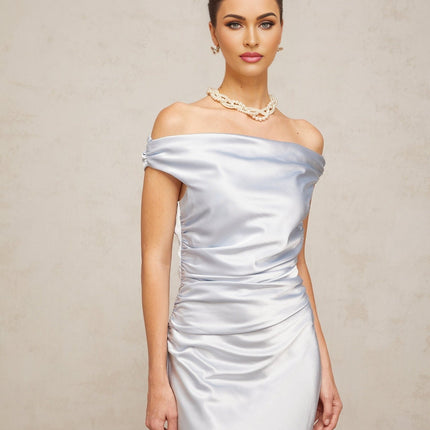 A woman wearing a blue offshoulder maxi dress with ruched satin fabric standing in a relaxed pose