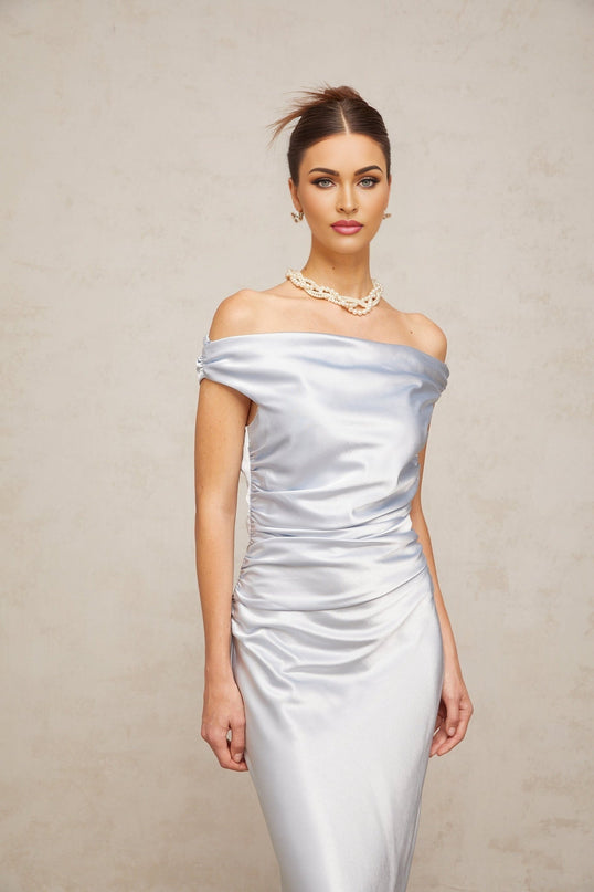 A woman wearing a blue offshoulder maxi dress with ruched satin fabric standing in a relaxed pose