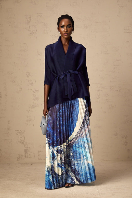 A woman wearing a blue patterned cape and matching skirt set The cape is creased and features a flowy design The skirt is form fitting The outfit has an all over print pattern in shades of blue