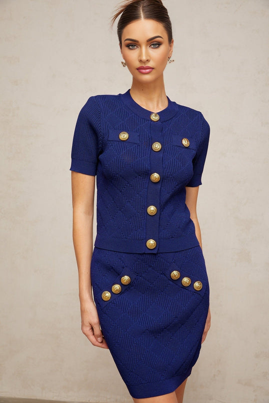 A woman wearing a blue plaid knit top and matching skirt set standing against a plain background The outfit features a checkered pattern in light and dark blue tones