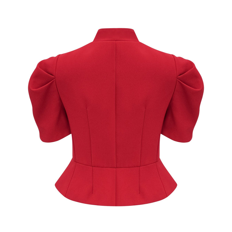 A woman wearing a bright red matching set consisting of a pleated blouse and skirt The blouse has long sleeves and a high neckline while the skirt falls to midi length with pleats throughout The outfit creates a stylish and coordinated look
