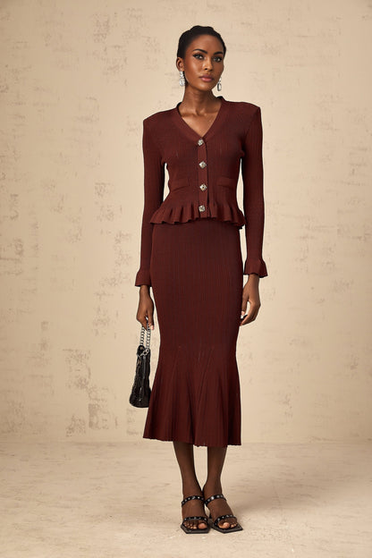 A woman wearing a bright red matching set consisting of a ruffled knit top and skirt The top features a sleeveless design with ruffle details while the skirt has a fitted silhouette Both pieces are made from a textured knit fabric creating a coordinated and stylish outfit